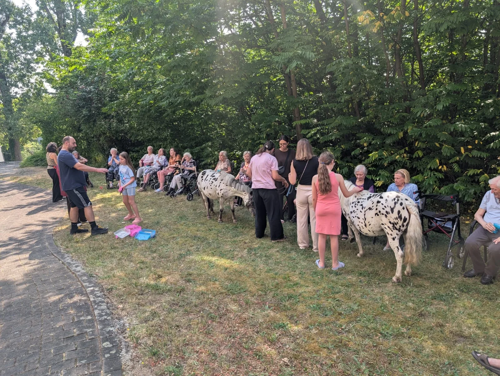 Bewohner im Halbkreis beim Ponybesuch auf dem Weg